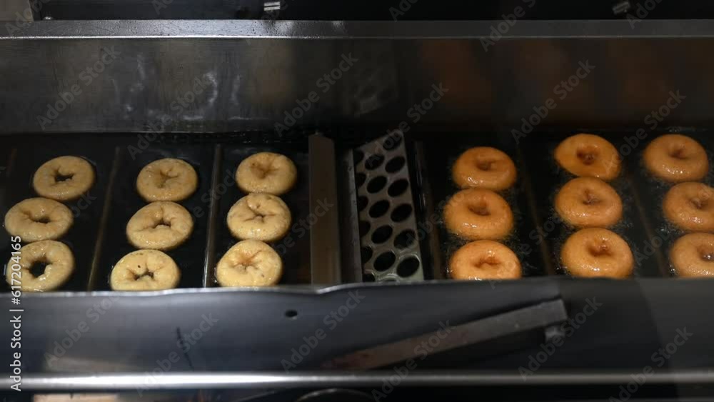 Mini donuts are flipped and fried in oil on an automated conveyor line. The machine flips donuts to the other side. Preparing fresh baked goods at the factory. Step 2