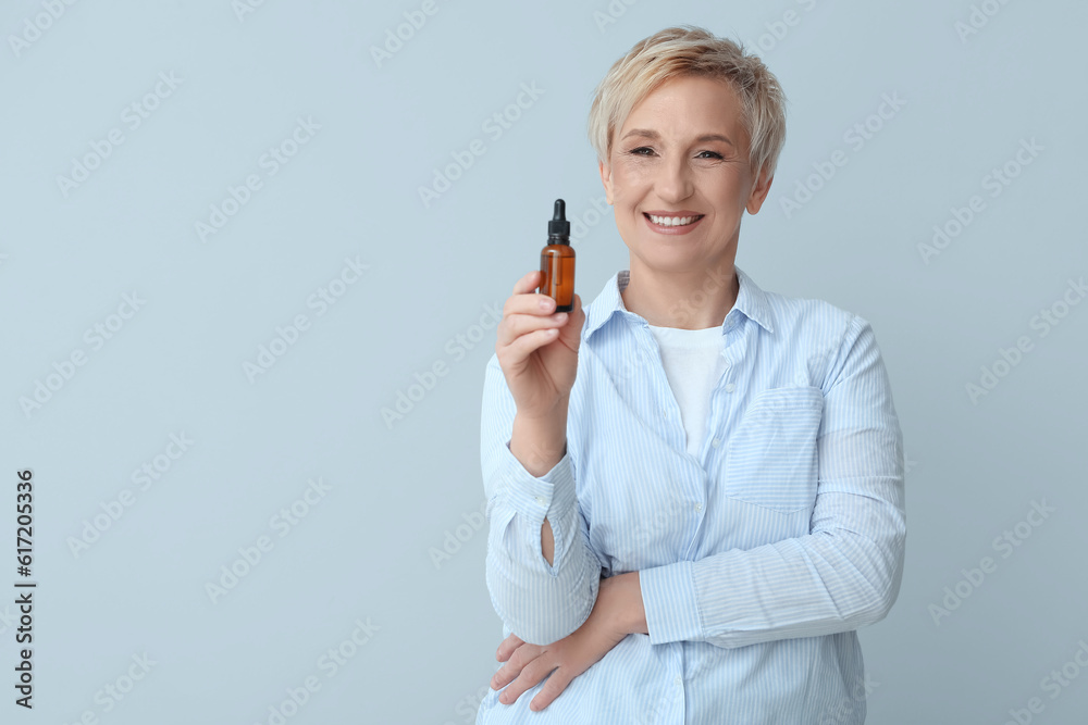 Mature woman with bottle of serum on light background Mature woman with bottle of serum on light background