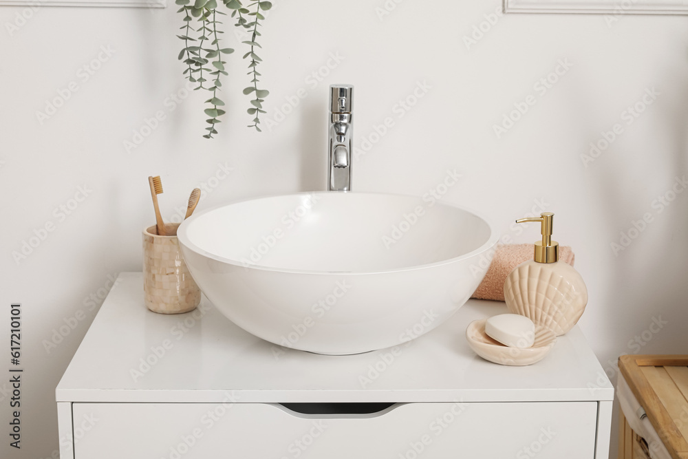 Fototapeta premium Sink bowl, soap bar, dispenser and cup with toothbrushes on chest of drawers in bathroom, closeup