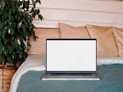 Laptop blank screen on bed in country house bedroom interior background, mockup, template. Clipping path device screen. Silver aluminium laptop at bed near green waringin tree in scandinavian country photo