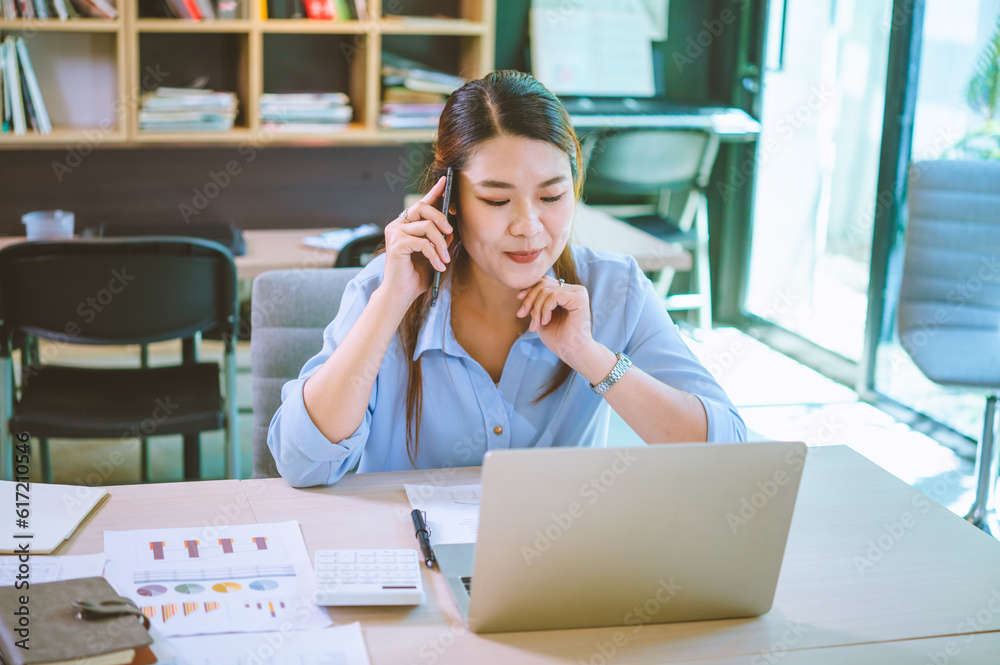 Business asian woman sitting at her desk with laptop using mobile phone chatting with customers or giving financial advice. Business asian woman sitting at her desk with laptop using mobile phone chatting with customers or giving financial advice.
