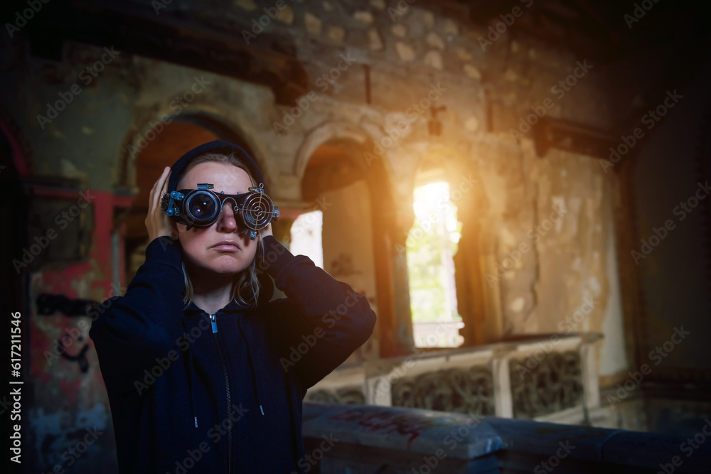 A blonde girl wearing steampunk glasses and a black hoodie in the doorway of an abandoned old building. A spectacular photo in the style of steam punk