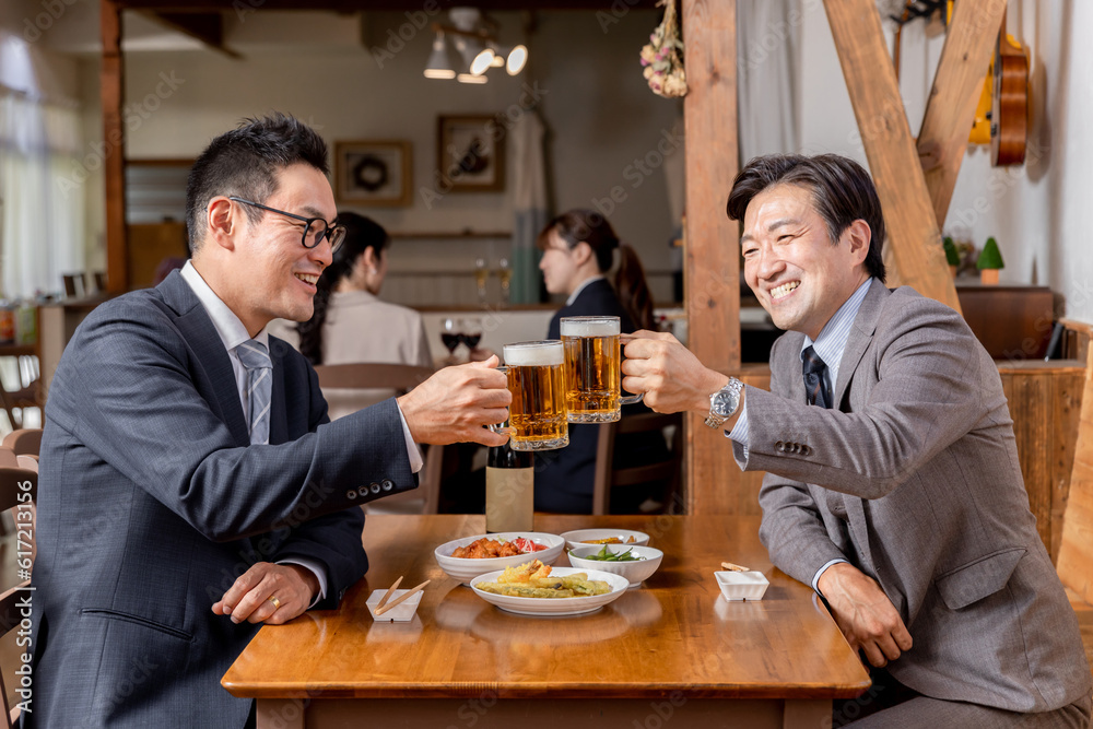 居酒屋で同僚・友達と飲み会・ビールで乾杯をするスーツ姿のビジネスマン・サラリーマンの男性
