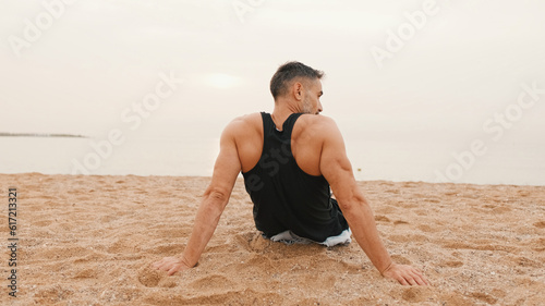 Middle-aged athletic man sits on the beach after workout and looks at the sea, Back view