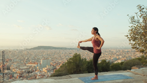 Girl practices yoga stands on one leg at lookout point at dawn