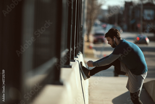 Young adult man tying his shoelaces while jogging in the city