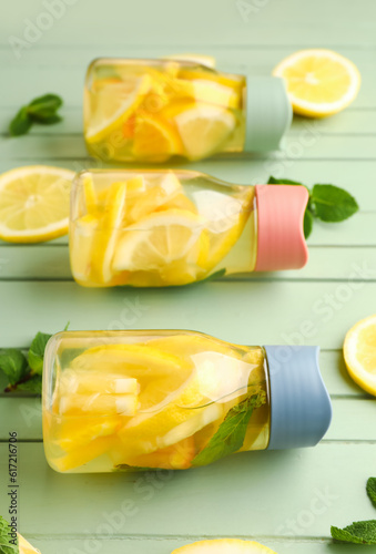 Sports bottles of infused water with lemon and mint on green wooden background