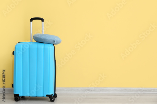 Blue suitcase with travel cushion near yellow wall. Travel concept