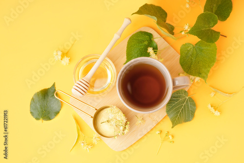 Cup of linden tea and bowl with honey on orange background