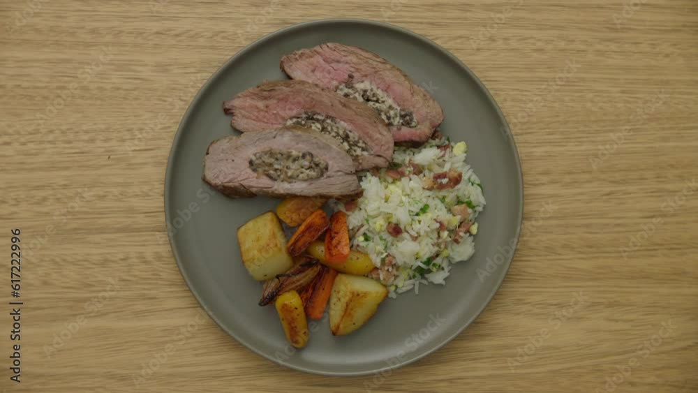 top view of a plate of seasoned rice, roasted vegetables, and three pieces of steak rotating top view of a plate of seasoned rice, roasted vegetables, and three pieces of steak rotating