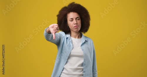 Upset unhappy africam american woman showing thumbs down Dislike sign gesture, expressing discontent, disapproval, dissatisfied isolated on orange studio background photo