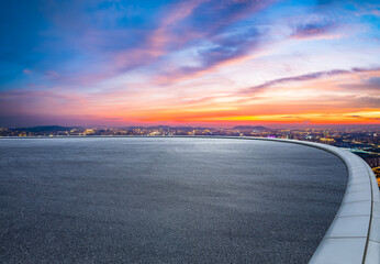 Round asphalt road and city skyline with colorful sky clouds at sunset