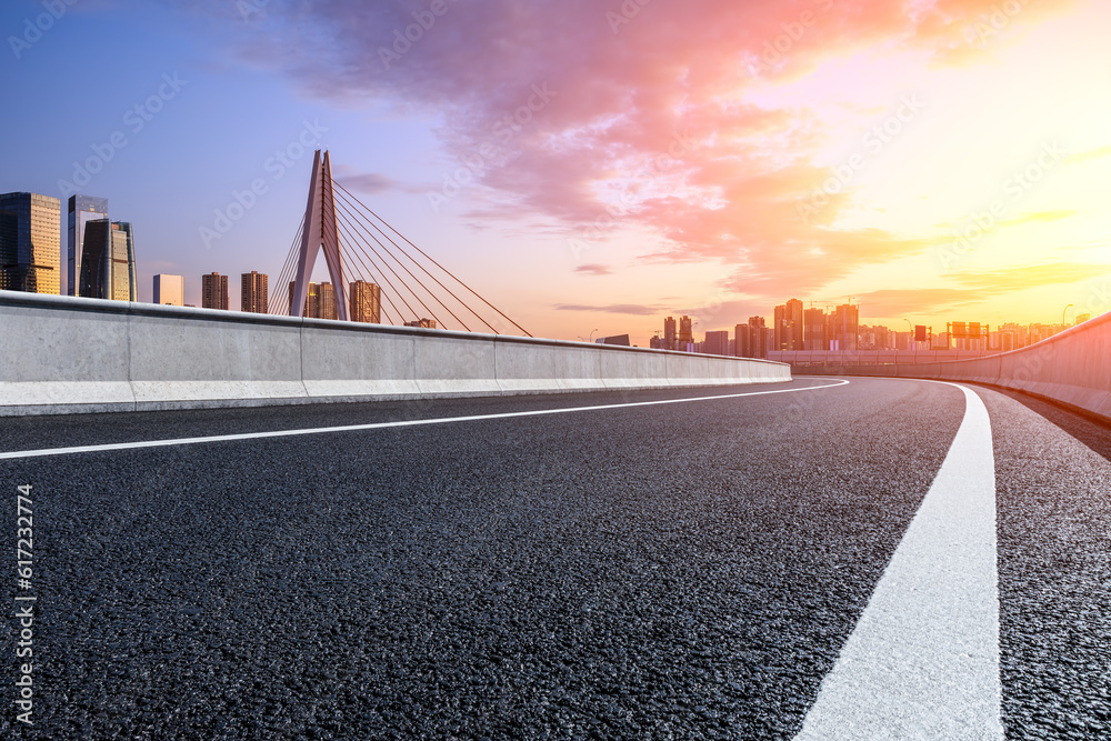Fototapeta premium Asphalt road and urban skyline with modern buildings at sunrise