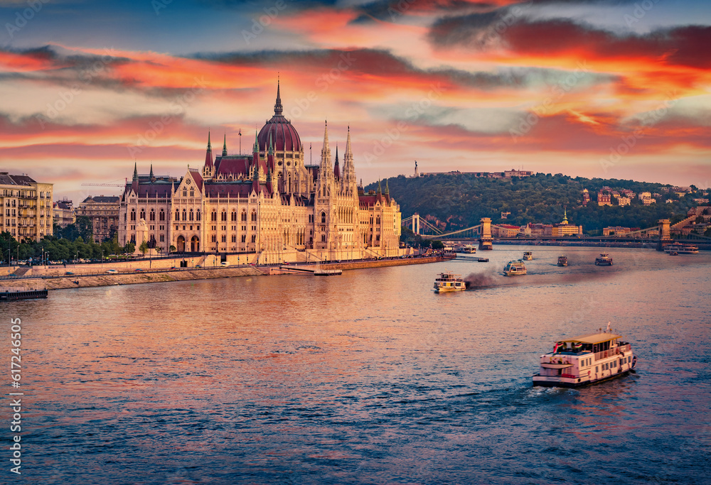 Naklejka premium Old pleasure boats on Dunabe river with Parliament house on background. Stunning summer cityscape of Budapest. Amazing sunset in Hungary, Europe. Traveling concept background.