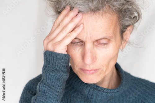 Close up head and shoulders view of older woman in blue sweater looking down with hand on head - pain concept (selective focus)