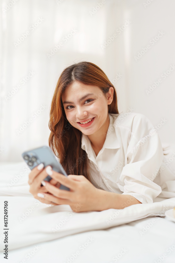 Happy smiling asian woman stretching on bed in the morning and holding mobile phone Happy smiling asian woman stretching on bed in the morning and holding mobile phone