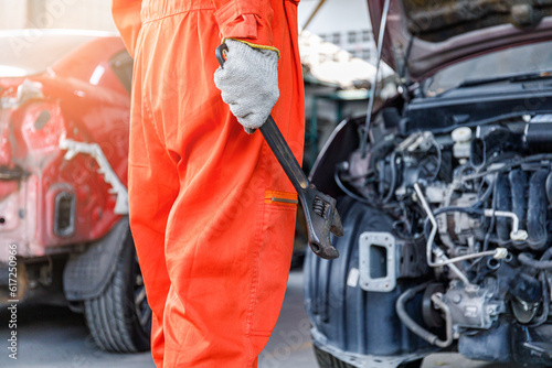 Side view of a male mechanic in orange clothes Craftsman holding a large wrench working in a car workshop