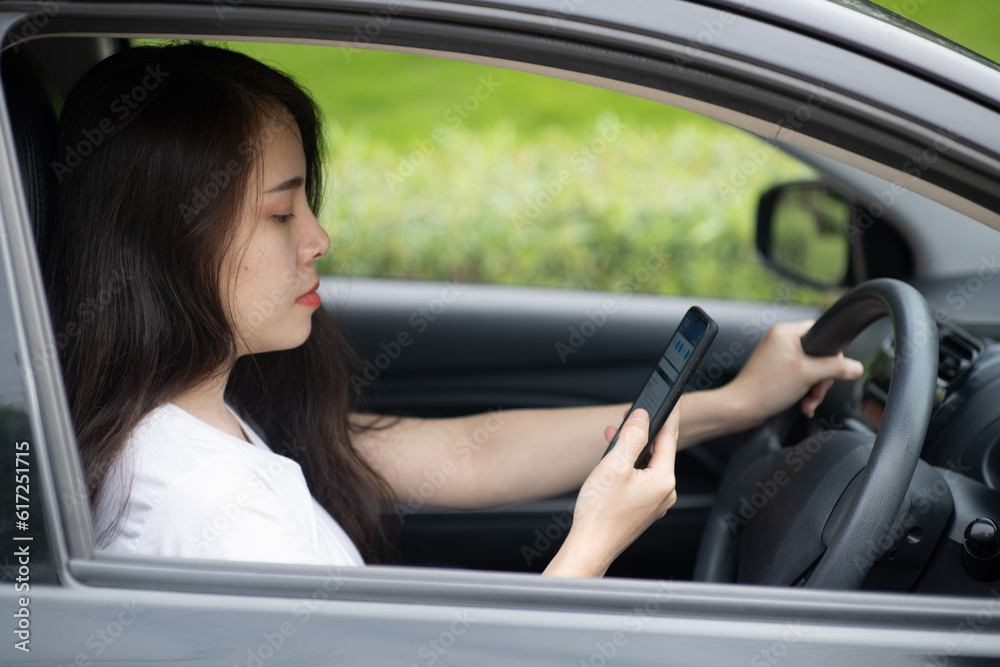 A woman driving a car looks at a mobile phone to see a map on the road.