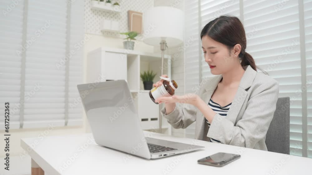 Asian business woman working with laptop and bring a bottle of vitamin to eat for health nourishment in office room. Healthcare and medical concept