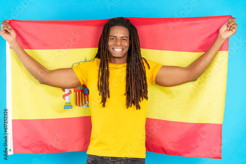 Happy latin man with dreadlocks raising a spanish national flag