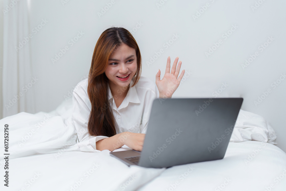 Happy smiling asian woman stretching on bed in the morning and using laptop computer Happy smiling asian woman stretching on bed in the morning and using laptop computer