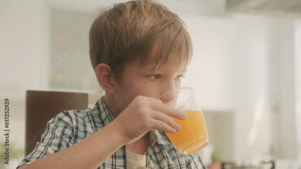 Child eating biscuit and drinking orange juice while watching cartoon on digital tablet at kitchen table and talking to mom Child eating biscuit and drinking orange juice while watching cartoon on digital tablet at kitchen table and talking to mom