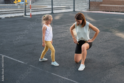 Mother and daughter go in for sports outdoors. Caucasian woman and little girl are engaged in fitness at the stadium.