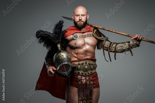 Schilderij op canvas Confident bald gladiator with light armor and red cape, holding a spear and glad