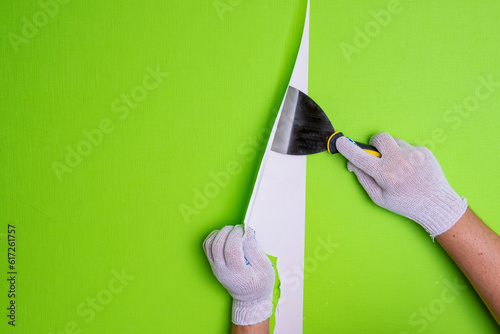 Men's gloved hands remove old wallpaper from the wall with a spatula. Background with hands doing repairs. The concept of repair and renovation.