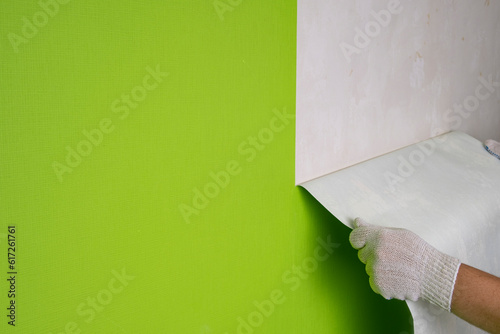 Gloved hands remove wallpaper from the wall in the room.