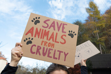 Hand holding placard sign with text Save animals from cruelty, during animal rights march. Protestor with cardboard banner at protest rally demonstration.