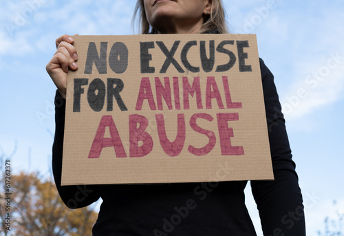Woman holding placard sign with text No Excuse for Animal Abuse, during animals rights march. Protestor with cardboard banner at protest rally demonstration.