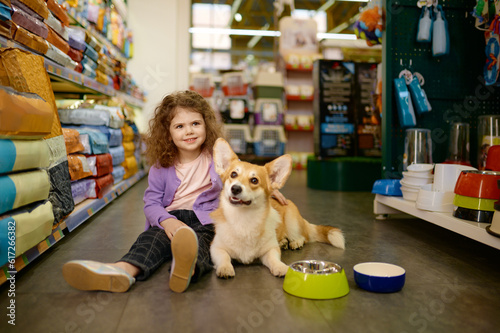 Little girl child sitting on pet shop floor holding corgi dog on knees