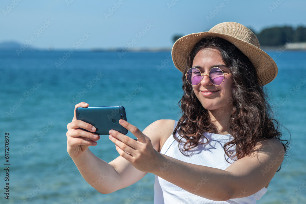 Fototapeta premium relaxed young woman taking a selfie or direct video with phone on the beach