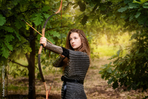 Medieval warrior woman in chain mail and bracers with a bow in her hands against the backdrop of an evening summer forest. photo