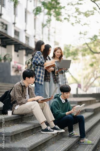 Asian Students are studying the campus park. Young people are spending time together. Reading book, working with laptop and tablet sitting on stairs