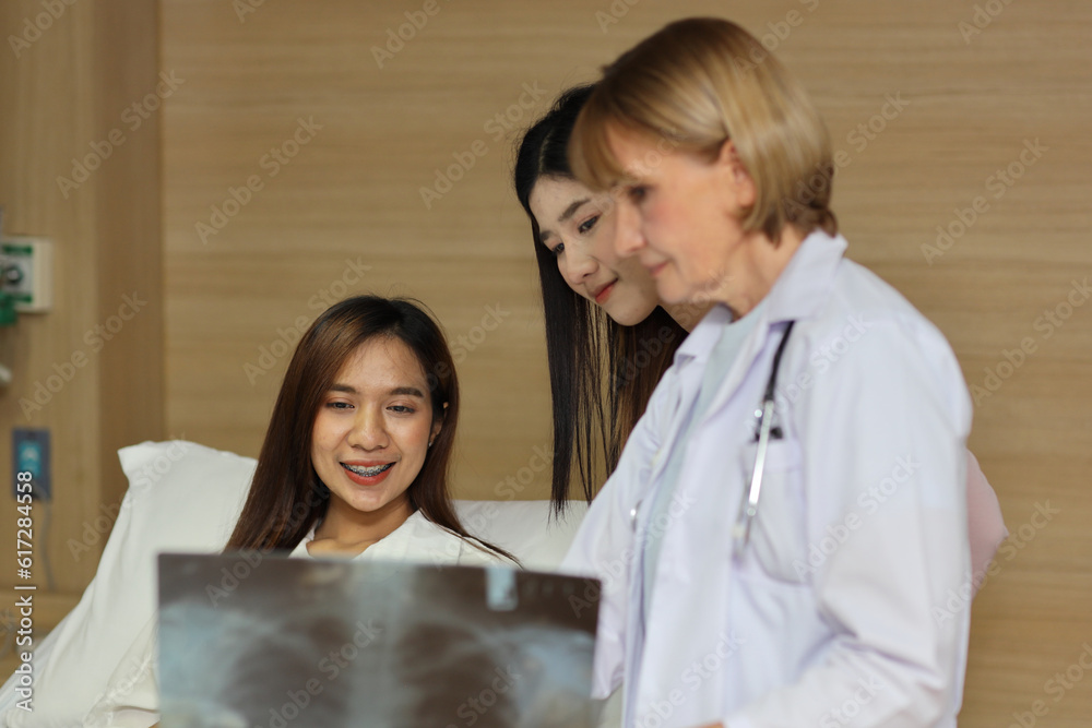 Female doctor greeting and showing happy patient and her friend with x-ray film after surgery in hospital room. Medical and insurance concept. Female doctor greeting and showing happy patient and her friend with x-ray film after surgery in hospital room. Medical and insurance concept.