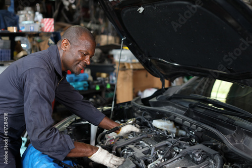 Man technician car mechanic in uniform checking maintenance a car service at repair garage station. Worker holding wrench and fixing breakdown vehicle. Concept of car center repair service.