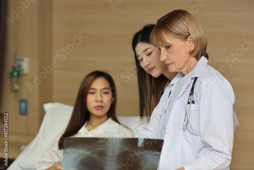 Female doctor greeting and showing happy patient and her friend with x-ray film after surgery in hospital room. Medical and insurance concept.
