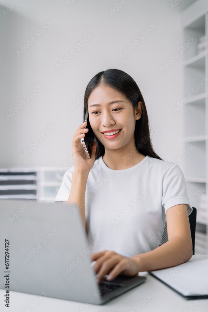 Portrait of Asian businesswoman talking mobile phone and working on laptop and papers on table in her office. Portrait of Asian businesswoman talking mobile phone and working on laptop and papers on table in her office.