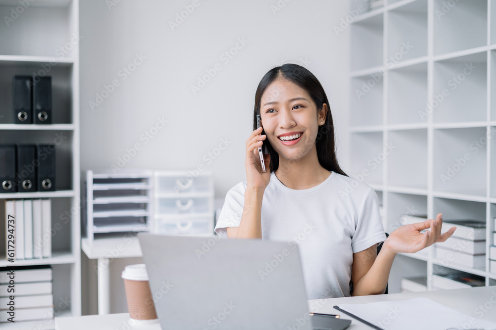 Portrait of Asian businesswoman talking mobile phone and working on laptop and papers on table in her office. Portrait of Asian businesswoman talking mobile phone and working on laptop and papers on table in her office.