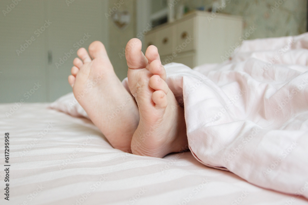 Feet under a light blanket on the bed. Concept of health Feet under a light blanket on the bed. Concept of health
