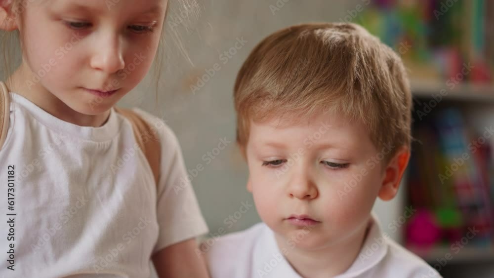 Concentrated little children play board game together in kindergarten closeup. Elder sister does homework with junior brother at home. Cute kids Concentrated little children play board game together in kindergarten closeup. Elder sister does homework with junior brother at home. Cute kids