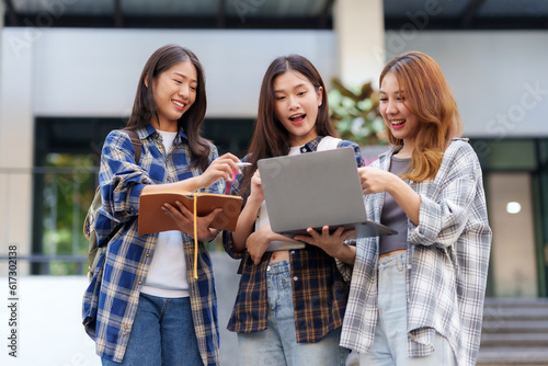 Cheerful group of Asian woman college students enjoying their studies Talk to friends outside of class using a laptop on campus. Concept of learning and education in the university.