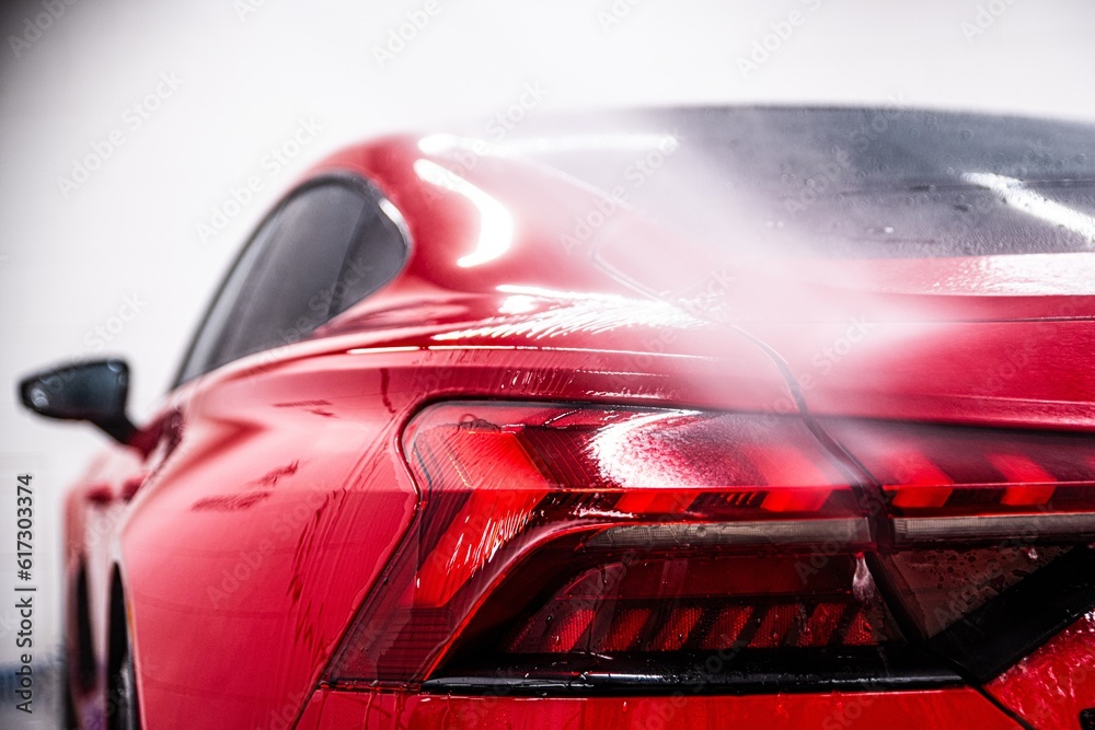 Washing a modern red car at a car wash using a pressure washer. Touchless washing.