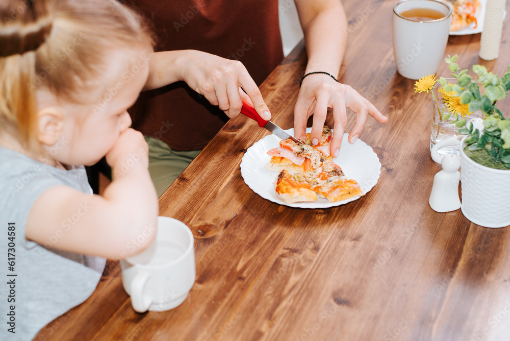 Close-up mom cuts homemade pizza, feeds her daughter in the kitchen Close-up mom cuts homemade pizza, feeds her daughter in the kitchen