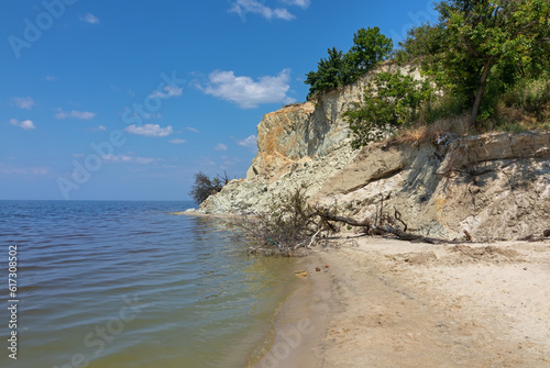 The collapsed steep bank of the Kremenchuk reservoir on the Dnieper river. Sandy beach near a hill with trees