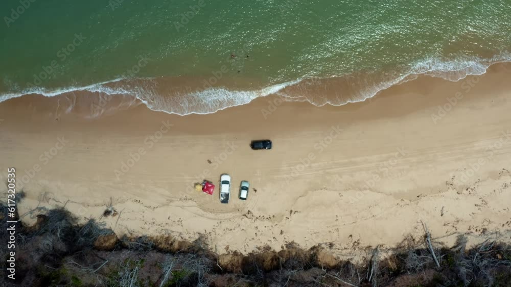 Aerial drone birds eye top view shot following a car drying down the tropical Malembá beach with golden sand and calm crystal clear turquoise water near Tibau do Sul in Rio Grande do Norte, Brazil Aerial drone birds eye top view shot following a car drying down the tropical Malembá beach with golden sand and calm crystal clear turquoise water near Tibau do Sul in Rio Grande do Norte, Brazil