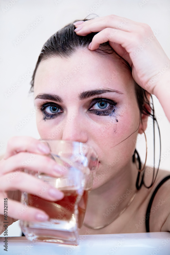 A young beautiful brunette with blue eyes, damp hair and heavily runny makeup drinks from a glass. A young beautiful brunette with blue eyes, damp hair and heavily runny makeup drinks from a glass.