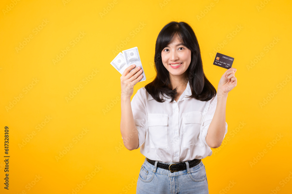 happy successful confident young asian woman happy smile wearing white shirt and denim jean holding cash money and credit card standing over yellow background. millionaire business, shopping concept. happy successful confident young asian woman happy smile wearing white shirt and denim jean holding cash money and credit card standing over yellow background. millionaire business, shopping concept.